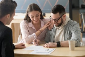 happy young couple buying a house for the first time and signing papers on closing day with agent