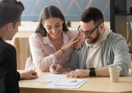 happy young couple buying a house for the first time and signing papers on closing day with agent