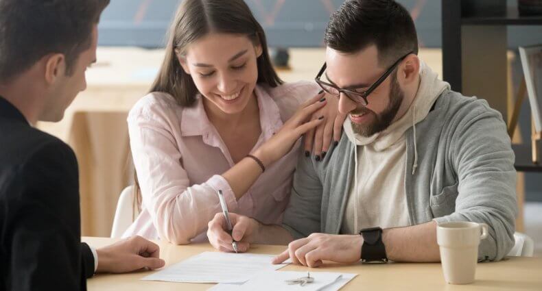 happy young couple buying a house for the first time and signing papers on closing day with agent