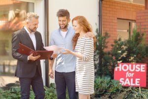Agent talking to a couple in front of a house for sale, sell your home concept