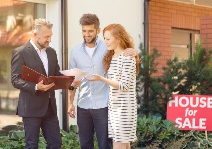 Agent talking to a couple in front of a house for sale, sell your home concept