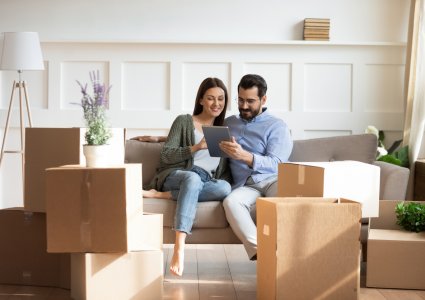 Couple sitting on a couch while using a tablet device to look for a property during their home buying process.