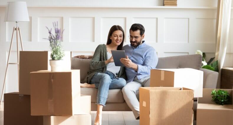Couple sitting on a couch while using a tablet device to look for a property during their home buying process.