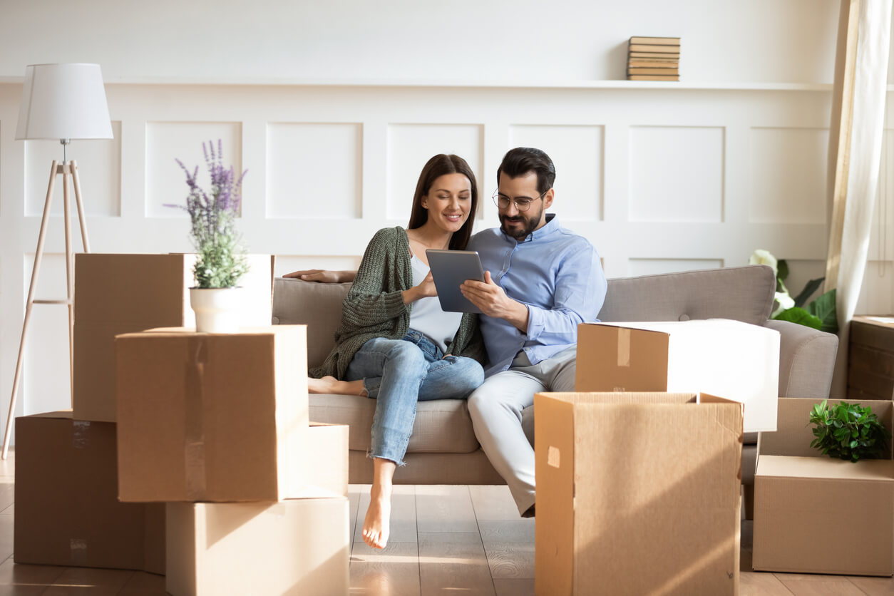 Couple sitting on a couch while using a tablet device to look for a property during their home buying process.