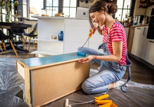 Smiling young woman painting a cabinet for her DIY home decor