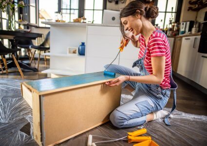 Smiling young woman painting a cabinet for her DIY home decor