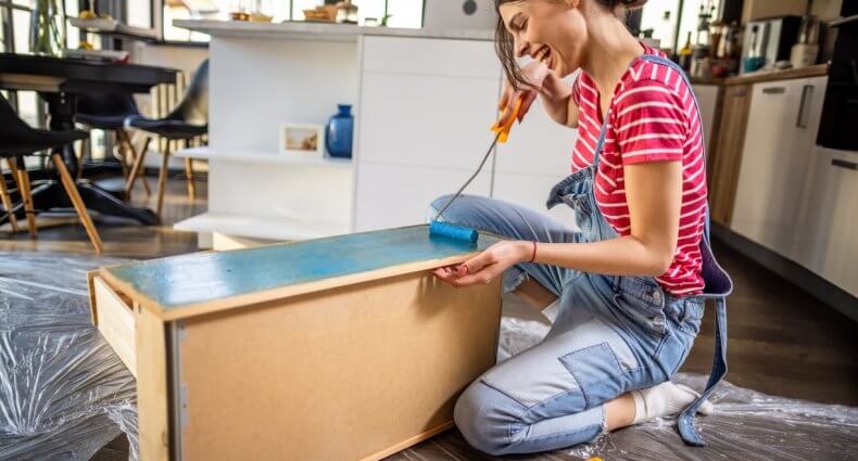 Smiling young woman painting a cabinet for her DIY home decor
